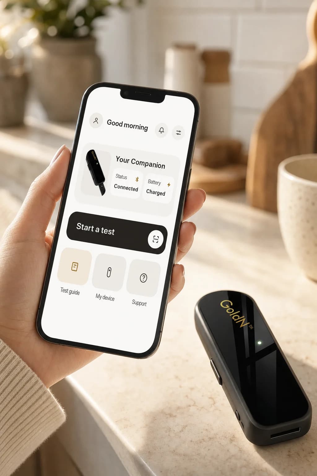 A hand holding a phone showing the GoldN Companion app home with connection and battery status