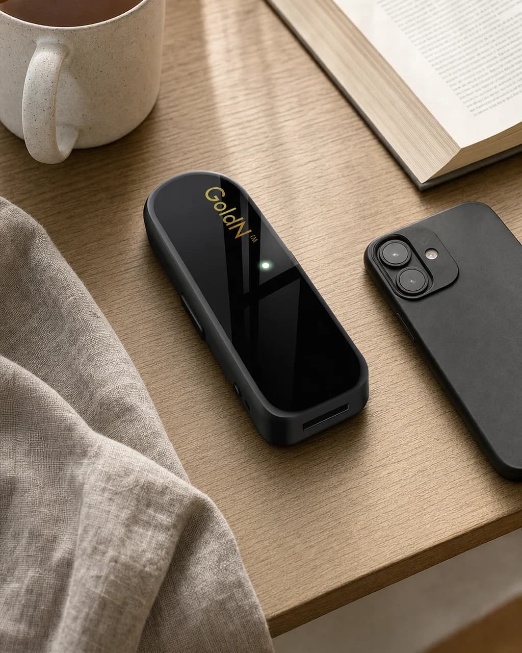The GoldN Companion on a wooden bedside table next to a mug, a book and a phone