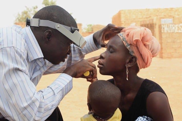 A health worker examines a patient outdoors in a community setting
